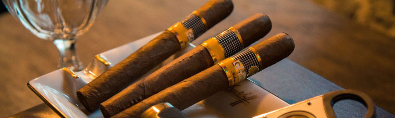 Trois cigares posés dans un récipient avec un coupe-cigare et un briquet sur une table en bois