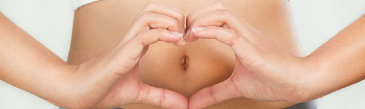 Une femme avec ses mains en forme de cœur sur le ventre pour signifier qu'elle est enceinte