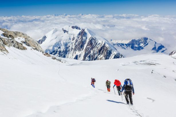 Une équipe de 4 personnes marchent à travers une plaine enneigée face à une montagne