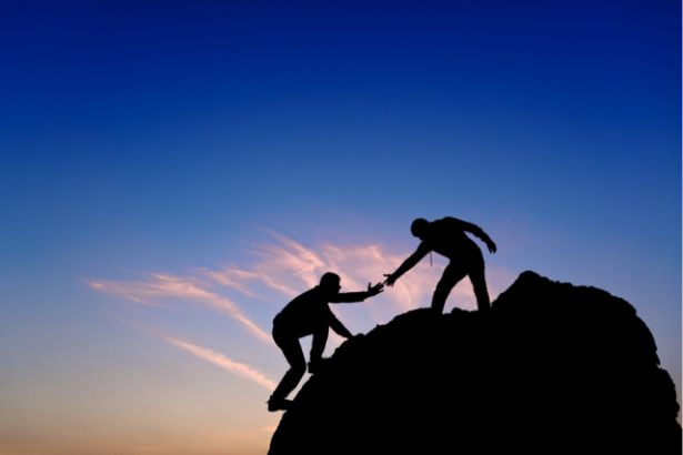Une personne aide une autre personne à atteindre le haut d'une montagne en la tenant par le bras