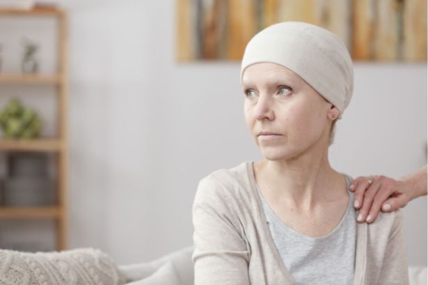 Une femme atteinte d'un cancer est assise sur un canapé, une main est posée sur son épaule comme pour la réconforter