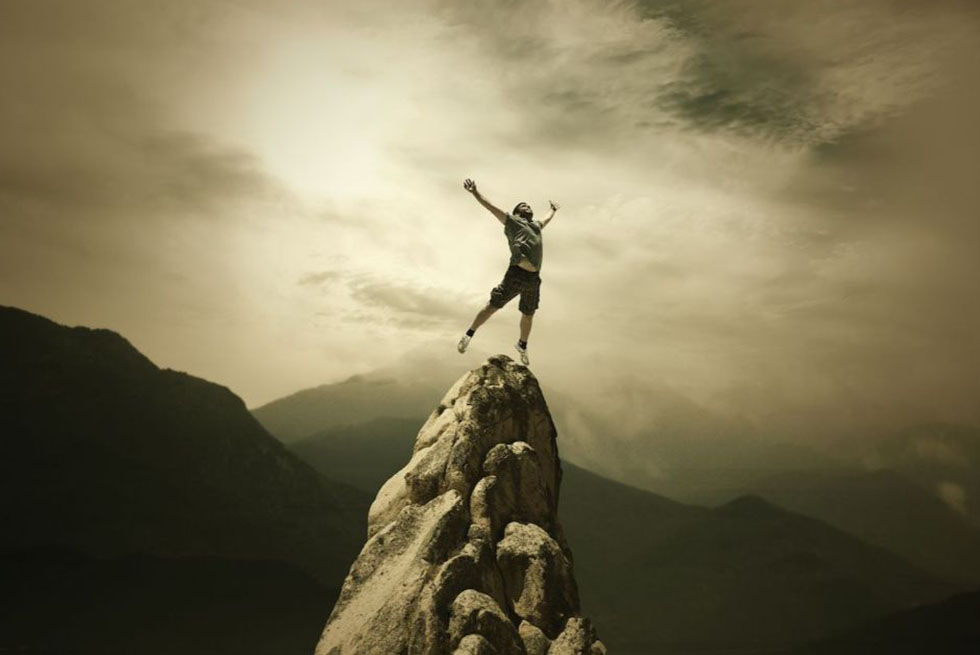 Un homme se tient debout en haut d'un pic rocheux, l'air victorieux