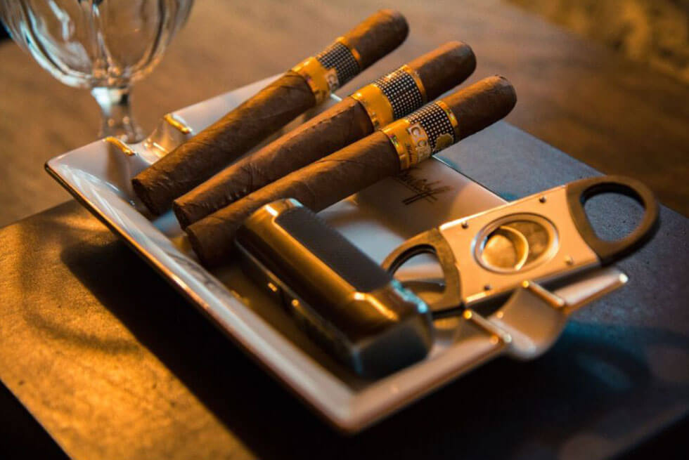 Trois cigares posés dans un récipient avec un coupe-cigare et un briquet sur une table en bois