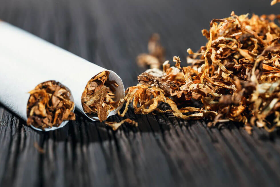 Une cigarette cassée en deux avec du tabac renversé à coté, sur une table en bois