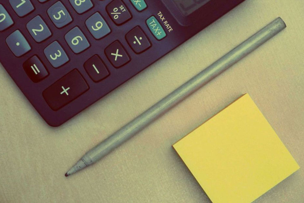 Une calculatrice, un stylo et un bloc de post-it sont posés sur un bureau