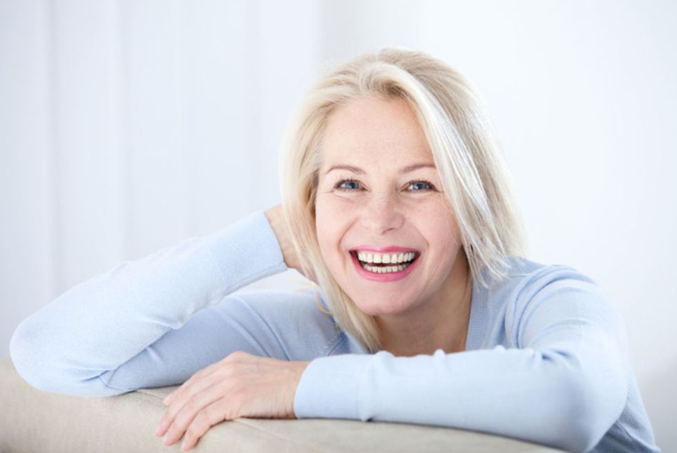 Une femme mûre souries en s'appuyant sur le dossier d'un canapé