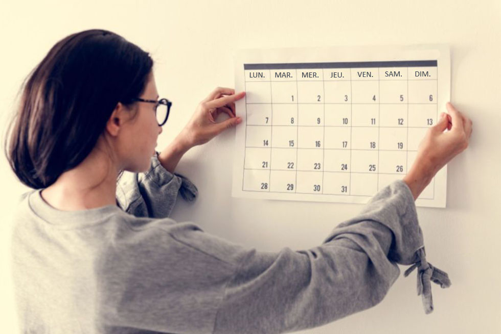 Une femme accroche un calendrier sur un mur blanc